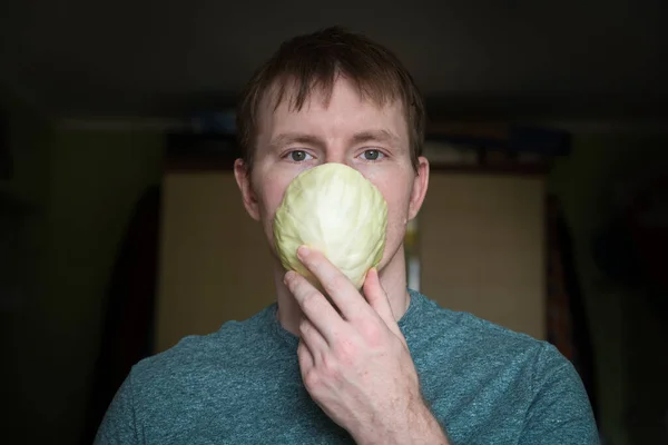 The young man covers his nose and mouth with a cabbage leaf instead of a medical mask. No masks protecting against infection and covid-19 during the coronavirus pandemic. Finished of funds to prevent infection.