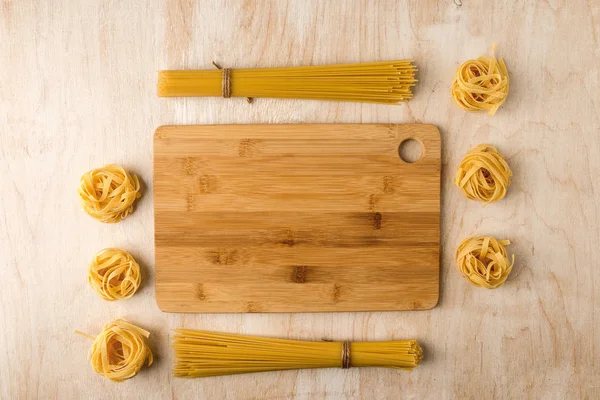 Spaghetti and fettuccine on a wooden background around a bamboo — Stock Photo, Image