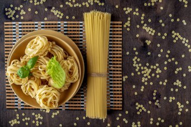 dry pasta decorated with fresh lettuce and Basil leaves on a yel