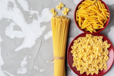 three types of pasta in a red ceramic dish on a textured gray ba