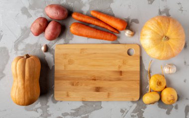 Çeşitli sebzeler gri bir kesim tahtasının etrafına dizilir.