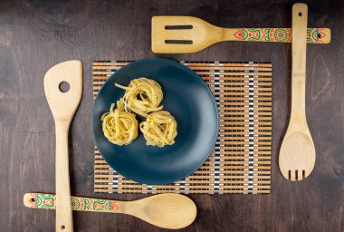 Bambu peçetenin üzerinde kuru fettucine macunu ve bambu bıçaklarla çevrili ahşap zemin, üst manzara, yazı için yer, düz makarna.