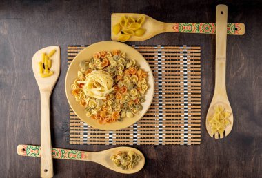 Bambu peçetedeki sarı seramik bir tabakta fettucine macunu ve ahşap arka planda farklı yapışık dört spatula, üst görünüm, yazı için yer, düz makarna.