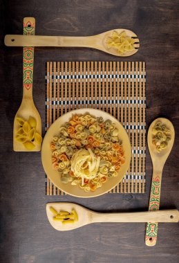 Bambu peçetedeki sarı seramik tabakta kuru fettucine macunu ve ahşap arka planda farklı yapıştırıcı içeren dört bambu spatulasından oluşan çerçeve, verittal çerçeve, üst manzara, yazı için alan, düz makarnalar.