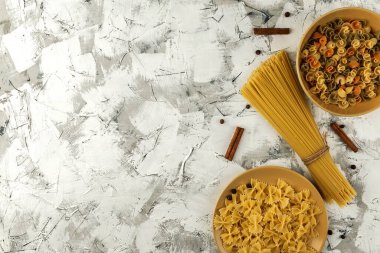 Rastgele renklendirilmiş beyaz-gri beton zemin üzerinde sarı seramik tabaklarda farklı makarna üst görünüm, yazı için yer düz makarna.