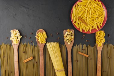 Kırmızı tabakta kuru makarna ve bambu teknelerinin üzerinde makarna ile spagetti siyah desenli arka plan, üst görüş, yazı için yer, düz makarna