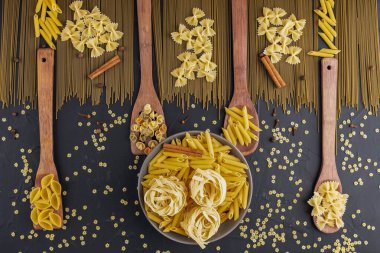 Gri seramik kâse ve çeşitli pastalar ve baharatlarla kaplı ahşap kaplar siyah dokulu arka plan, üst manzara, metin alanı, düz geçmiş yatıyordu