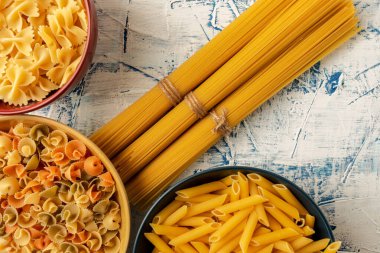 Yumuşak desenli beyaz-mavi arka planda farklı pastalardan yapılmış çok renkli seramik tabaklar ile spagetti paketleri, üst görünüm, düz makarna