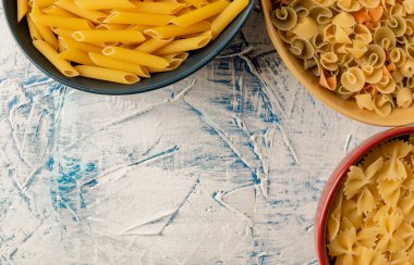 yumuşak-bulanık desenli beyaz-mavi zemin üzerinde çeşitli pastalar bulunan çok renkli seramik tabaklar, üst görünüm, metin alanı, düz makarnalar