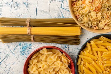 Demet demet spagetti ve mavi ve beyaz desenli arka planda çok renkli seramik kaselerde çeşitli pastalar. Uzun vadeli depolama ürünleri. Yukarıdan manzara, düz makarna.