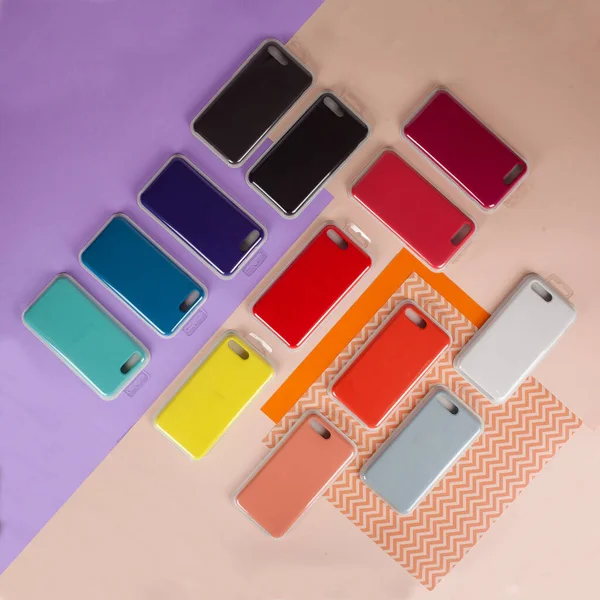 Cell phone cases various colors on multicolor paper background — Stock Photo, Image