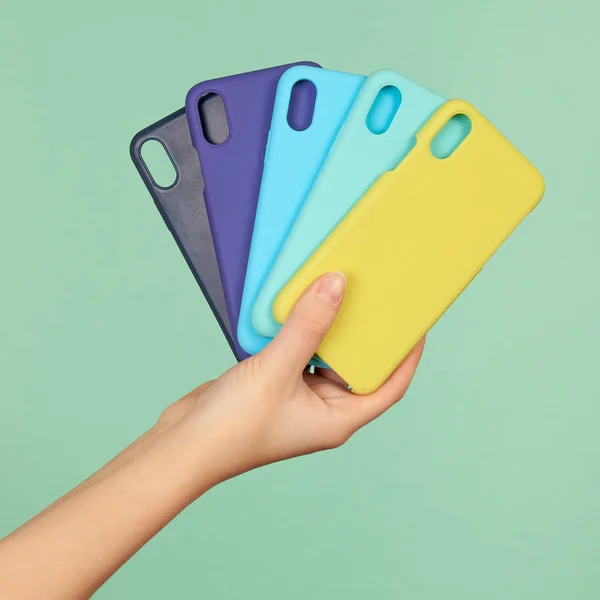 Hand houdt de gekleurde covers gevallen voor de telefoon zwart, blauw, geel op de groene achtergrond — Stockfoto