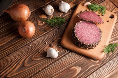 Eski ahşap bir masada tütsülenmiş salam. Biberiye, sarımsak ve biberli sosis.