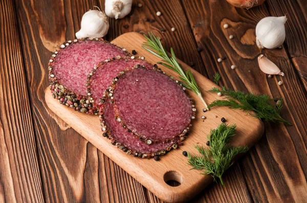 Salami ahumado en una vieja mesa de madera. Embutidos con romero, ajo y pimienta — Foto de Stock