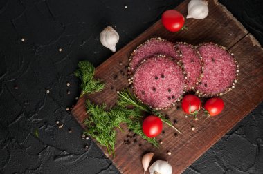 Siyah bir tablo ve bir kahverengi tahta üzerinde füme salam. Biberiye, sarımsak ve biber ve domates kiraz, dereotu, maydanoz ile sosis.