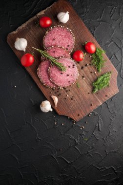 Siyah bir tablo ve bir kahverengi tahta üzerinde füme salam. Biberiye, sarımsak ve biber ve domates kiraz, dereotu, maydanoz ile sosis.