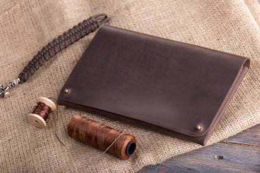 koyu ahşap arka plan üzerinde bir iş parçacığı ve bir iğne ile deri koyu kahverengi çanta.