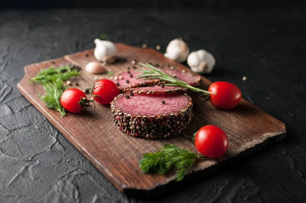 Siyah bir tablo ve bir kahverengi tahta üzerinde füme salam. Sosis ile 