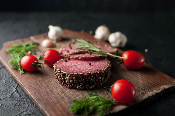 Siyah bir tablo ve bir kahverengi tahta üzerinde füme salam. Sosis ile 