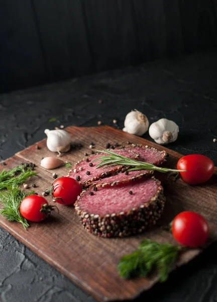 Siyah bir tablo ve bir kahverengi tahta üzerinde füme salam. Sosis ile 