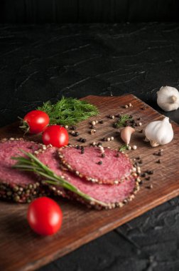 Siyah bir tablo ve bir kahverengi tahta üzerinde füme salam. Sosis ile 