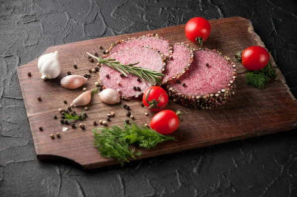 Gerookte salami op een zwarte lijst en een bruin bord. Worstjes met — Stockfoto