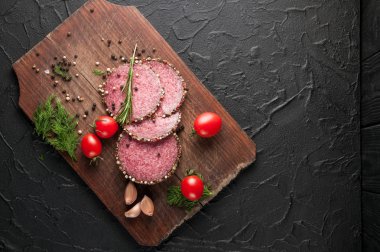 Siyah bir tablo ve bir kahverengi tahta üzerinde füme salam. Sosis ile 