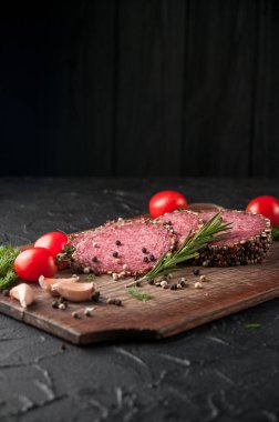 Siyah bir tablo ve bir kahverengi tahta üzerinde füme salam. Biberiye, sarımsak ve biber ve domates kiraz, dereotu, maydanoz ile sosis.