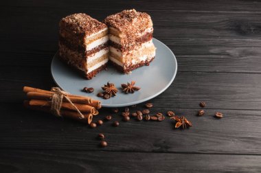 Şekerli tatlı tiramisu baharat siyah bir ahşap zemin üzerinde gri bir plaka üzerinde bir kesim içinde: tarçın ve badan, kahve çekirdekleri.