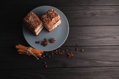 Şekerli tatlı tiramisu baharat siyah bir ahşap zemin üzerinde gri bir plaka üzerinde bir kesim içinde: tarçın ve badan, kahve çekirdekleri.
