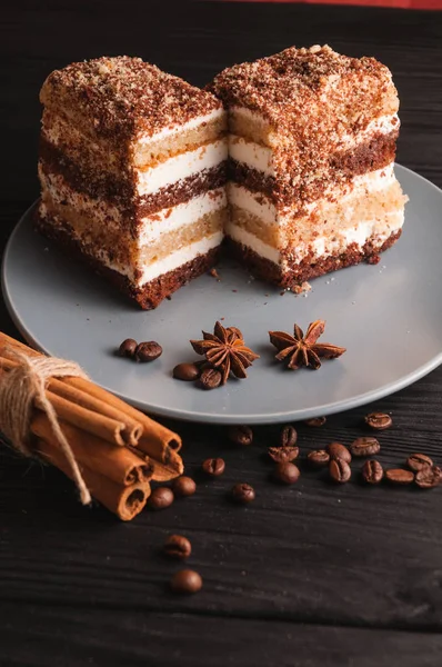 Sweet dessert tiramisu in a cut on a gray plate on a black wooden background with spices: cinnamon sticks and badan, coffee beans. — Stock Photo, Image