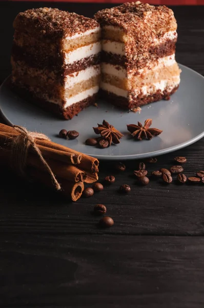 Sweet dessert tiramisu in a cut on a gray plate on a black wooden background with spices: cinnamon sticks and badan, coffee beans. — Stock Photo, Image