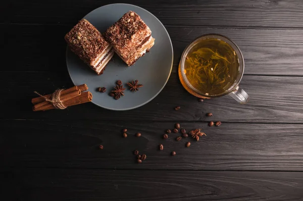 Dos piezas de pastel de miel de varias capas en un plato, sobre un fondo de madera negro con una taza de té, palillos y granos de café, vista superior . — Foto de Stock