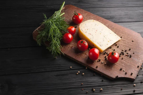 Peynir kahverengi ahşap tahtası üzerinde siyah bir ahşap arka plan, cherry domates, biber, yeşillik, baharat, dereotu, maydanoz. Yukarıdan görüntülemek.