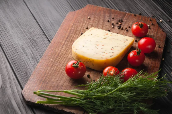 Peynir kahverengi ahşap tahtası üzerinde siyah bir ahşap arka plan, cherry domates, biber, yeşillik, baharat, dereotu, maydanoz. Yukarıdan görüntülemek.