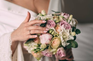 Gelin elinde pembe bir gelin buketi tutuyor, buket pembe bir kurdeleyle bağlanmış. Gelin güzel beyaz bir bornoz giyiyor.