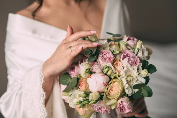 新娘手里拿着一束粉红色的新娘新娘花束，花束用粉色缎带捆扎。新娘穿着漂亮的白色浴衣 免版税图库照片