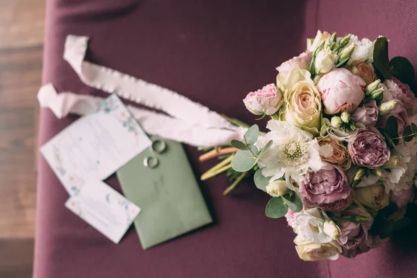 O buquê de casamento da noiva em estilo rosa, o buquê é amarrado com uma fita rosa, ao lado dele são convites e alianças de casamento — Fotografia de Stock