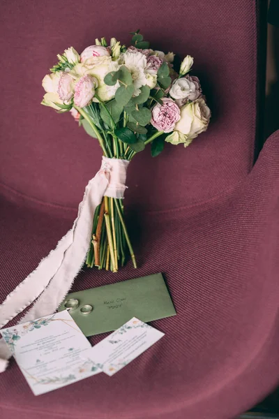 新娘的结婚花束是粉红色的，花束上系着粉红色的缎带，旁边是邀请函和结婚戒指 免版税图库图片