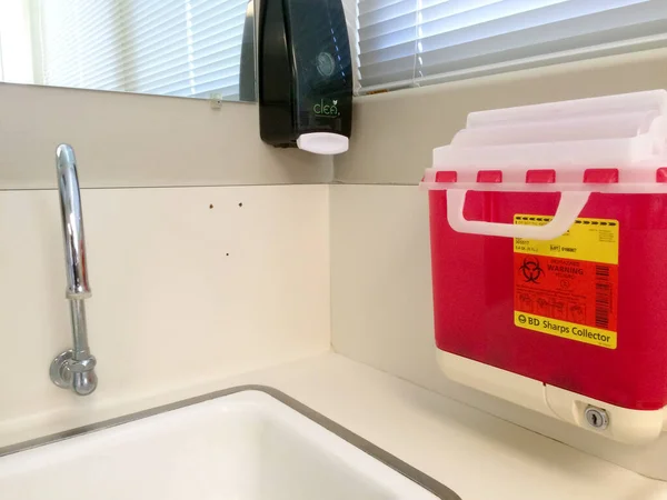 Sharps kolektor biohazard červený kontejner v blízkosti dřezu a mytí rukou mýdlo — Stock fotografie