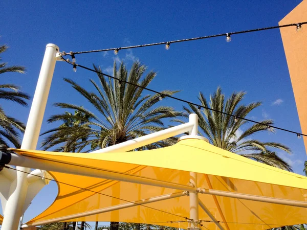 Canopias de sombra amareladase palmeiras no dia ensolarado — Fotografia de Stock