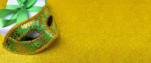 Ornate carnival mask, gift box on glitter golden background. Mardi gras festive celebration banner with copy space.
