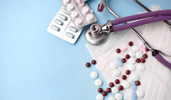 Spilling pills, medicine masks, stethoscope on blue background. Illness preventation or medical health care concept. Copyspace.