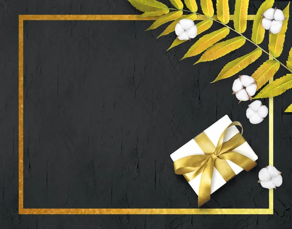 Gift box, cotton flowers and leaf  on black textured background. Golden frame mock up composition for luxury products presentation. Greeting holiday concept for Valentines day, Mothers day, Womans day or wedding celebration.