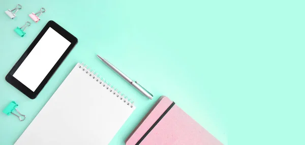 Feminine office flatlay with empty notepad, smartphone and stationery on mint background.  Online education or blogging concept. Trendy design. . Header with copy space