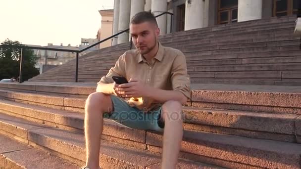 Ο άνθρωπος που κάθεται σε σκαλοπάτια, χρησιμοποιώντας το smartphone — Αρχείο Βίντεο