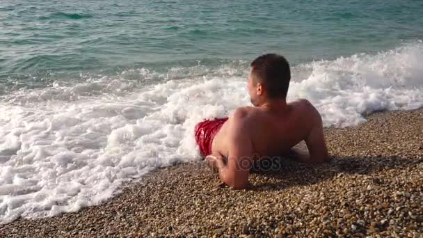 Knappe man ligt aan het strand in het water — Stockvideo