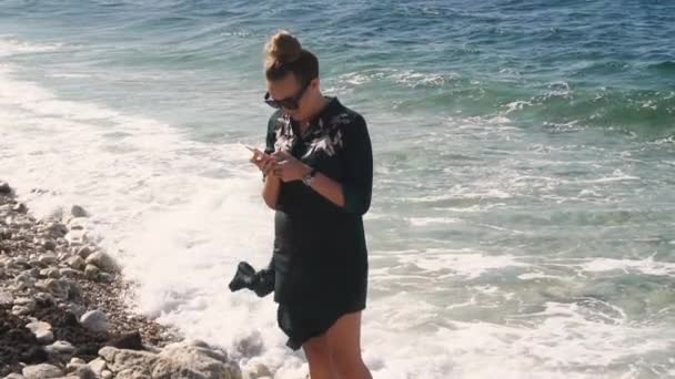 Mujer SMS mensajes de texto utilizando la aplicación en el teléfono inteligente en la playa puesta de sol . — Vídeo de stock