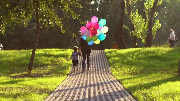 Mãe e filho estão andando ao longo da estrada em um parque com bolas coloridas, um olhar das costas — Vídeo de Stock