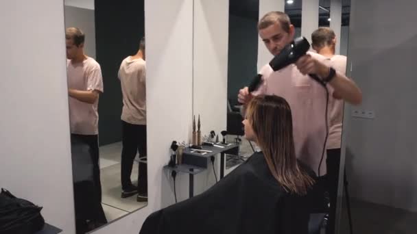 Professionele kapsalon gebruikt een haardroger. Jonge vrouw om haar haar gekleed in de kapsalon. Mannelijke stylist met een haardroger. Kapper met een föhn. Stapelen. Kapper op het werk. — Stockvideo